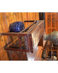 Wood low table with carved detail, blue ceramic piece, and green vase on polished wood floor, cabinets behind.