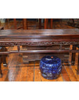 Brown carved wood low table beside a small blue ceramic stool on wooden flooring.