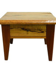 Natural mango wood side table with four legs, front drawer, and brass pull, shown in a close-up view.