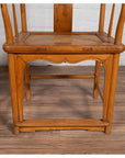 Brown wood and rattan Ming Dynasty style wedding armchair with curving arms on light brown floor by white brick wall.