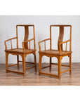 Brown wood and rattan armchairs with curved arms on a wooden floor against a white brick wall indoors.
