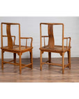 Brown wood and rattan armchairs with curved arms, pair set on wooden floor against a white brick wall indoors.
