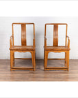 Brown wood and rattan Ming Dynasty style armchairs with curved arms, side by side on wooden floor indoors.