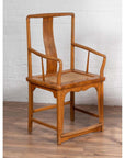 Brown wood and rattan armchair with curved arms, placed indoors against a white brick wall.