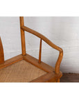 Close-up of brown wooden Ming Dynasty style wedding armchair with curved arms and rattan seat indoors.