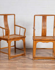 Brown wood and rattan Ming dynasty style wedding armchairs with curved arms, on a wooden floor by a white wall indoors.