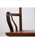 Close-up of brown wooden chair arms and seat with curved design, set indoors against a white brick wall.