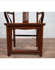 Brown wooden Ming Dynasty style wedding chair with carved medallion and curved arms on a wooden floor indoors.