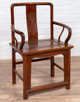 Brown wooden wedding chair with carved medallion and curving arms, placed on wood floor by a white brick wall indoors.