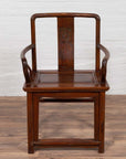 Brown wooden Ming Dynasty style wedding chair with carved medallion and curving arms on a wooden floor indoors.