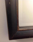 Close-up of dark brown wood mirror frame corner against a light-colored wall.