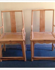 Natural wood chairs with tall, straight backs and armrests on blue carpet against a light wall, side by side.