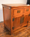 Natural wood small cabinet with two drawers, hinged doors, and unique hardware on wooden floor.