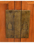 Close-up of two brass handles on natural wood cabinet, showing wood grain texture and visible screws.