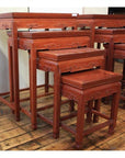 Four rosewood nesting tables with ornate carvings on a wooden floor against a cream-colored wall.