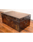 Large black lacquered trunk on wooden floor against a white wall, decorative storage furniture in home setting.
