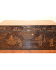 Black lacquer trunk with gold motifs and round metal clasp on a wooden floor.