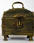 Gold-colored brass miniature treasure box with handle, latch, four legs, intricate patterns, close-up view.
