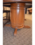Close-up of dark wood pedestal dining table base with four feet on a light carpeted floor.