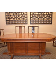 Brown wood oval pedestal dining table with matching chairs, set in a room with modern wall art.