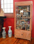 Brown teak display cabinet with glass doors, displaying figurines and blue and white vases, Thai statue beside.