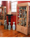 Vintage teak display cabinet from Thailand with ceramics inside, large vases and a statue in front on wood floors.