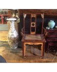 Light wood and rattan arm chairs beside a tall painted vase, blue jar, and nested tables on wooden floor.