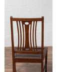 Brown wood Indonesian side chairs with pierced splats on wooden floor against white brick wall, indoors.