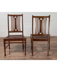 Brown wooden vintage Indonesian side chairs with pierced splats on a wooden floor by a white brick wall indoors.