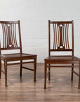 Brown wooden Indonesian side chairs with pierced backs, mid-century style, indoors by white brick wall and wood floor.