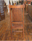 Teak armless chairs with vertical slat backrests on a wooden floor in an antique furniture store.