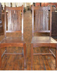 Brown teak armless chairs on indoor wooden floor, side by side, close-up view.
