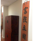 Brown wooden Chinese signs wall art on vertical panels, displayed in a bright hallway with white walls and wood cabinet.