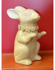 White porcelain bunny rabbit statue with a flower collar, set against a solid red background, close-up view.
