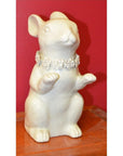 White porcelain bunny rabbit statue with floral necklace, sitting on wood, red background, close-up view.