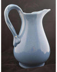 Close-up of a glossy blue crackle porcelain pitcher with curved handle against a plain dark background.