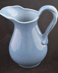 Close-up of blue crackle-glazed porcelain pitcher with curved handle against a black background.