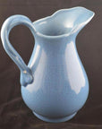 Close-up of crackle blue porcelain pitcher with curved handle and flared spout, set against a black background.