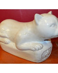 White porcelain reclining cat figure on a wooden base with a vibrant red wall background, close-up view.