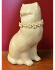 White porcelain cat figurine with head turned to the side on a wooden surface, red wall in background.