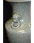 Close-up of green celadon porcelain vase with crackle glaze, featuring sculpted lion ring handle detail.