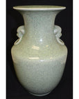 Light green crackle celadon porcelain vase with lion ring handle, close-up against black background.