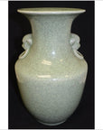 Light green crackle celadon porcelain vase with lion ring handle, close-up against black background.