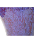 Close-up of purple, blue, and red glazed ceramic vase with textured surface on white background.