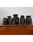 Brown wooden ghee pots on a chest against a white brick wall indoors.