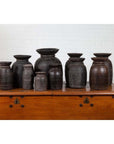 Brown wooden ghee pots in varying sizes on a chest, set against a white brick wall, rustic style.
