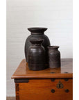Brown wooden ghee pots on wooden chest, white brick wall background, rustic Nepalese style, indoors.
