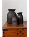 Brown wooden ghee pots on a chest against a white brick wall indoors.