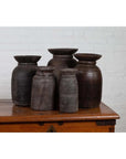 Brown wooden ghee pots set of five on a wooden chest, white brick wall background, indoors.