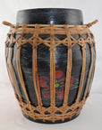 Close-up of a black ceramic jar with red flower design in a rattan and bamboo lidded basket with handles.